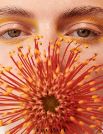 Close-up beauty shot of a face with yellow eyeshadow and eyebrows, with a protea flower covering the lower half of the face.