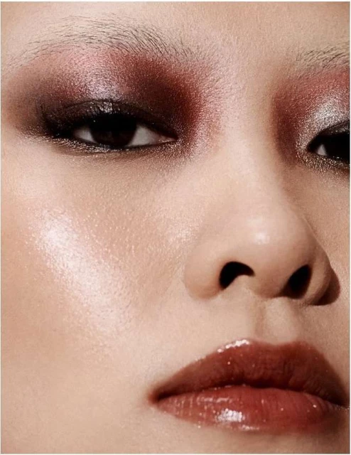 Close-up of a woman's face with dramatic, shimmering brown eyeshadow and glossy lips, highlighting beauty and makeup artistry.