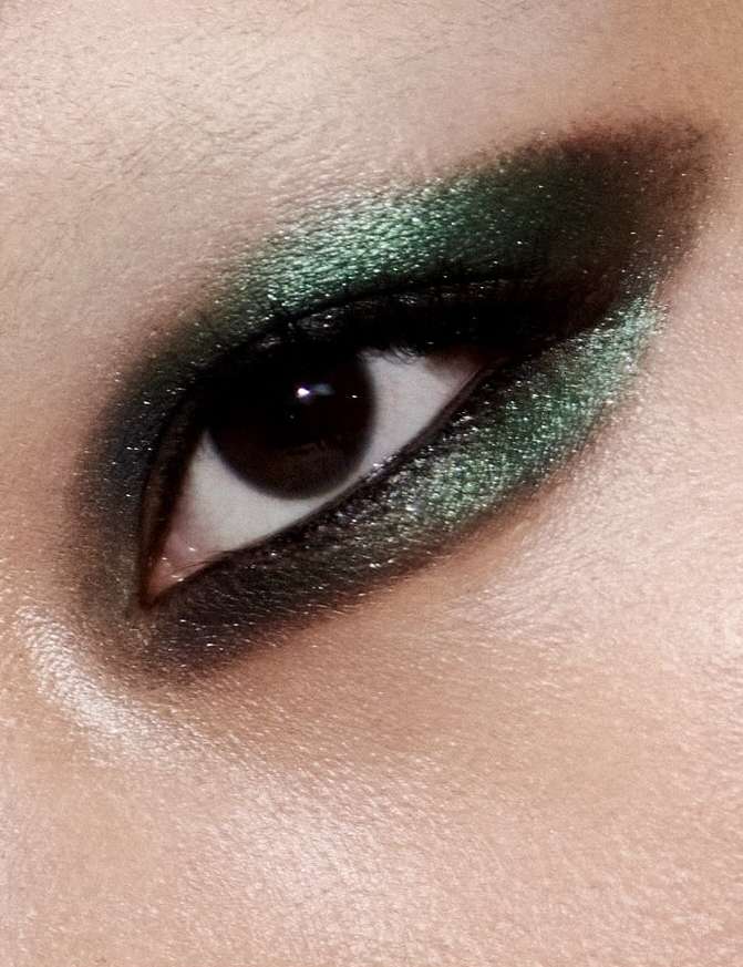 Close-up shot of a woman's eye with dark green eyeshadow and visible eyebrow, skin, and eyelashes, showcasing makeup.