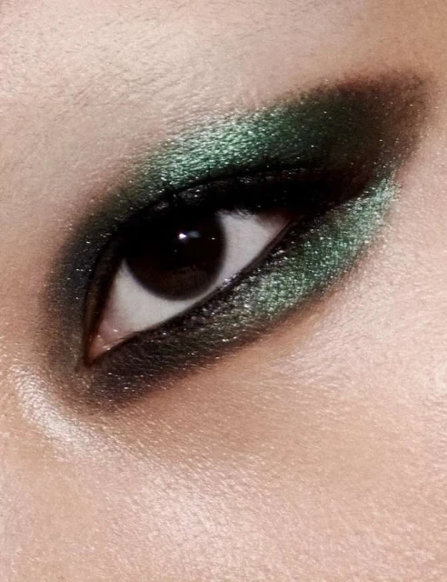 Close-up shot of a woman's eye with dark green eyeshadow and visible eyebrow, skin, and eyelashes, showcasing makeup.