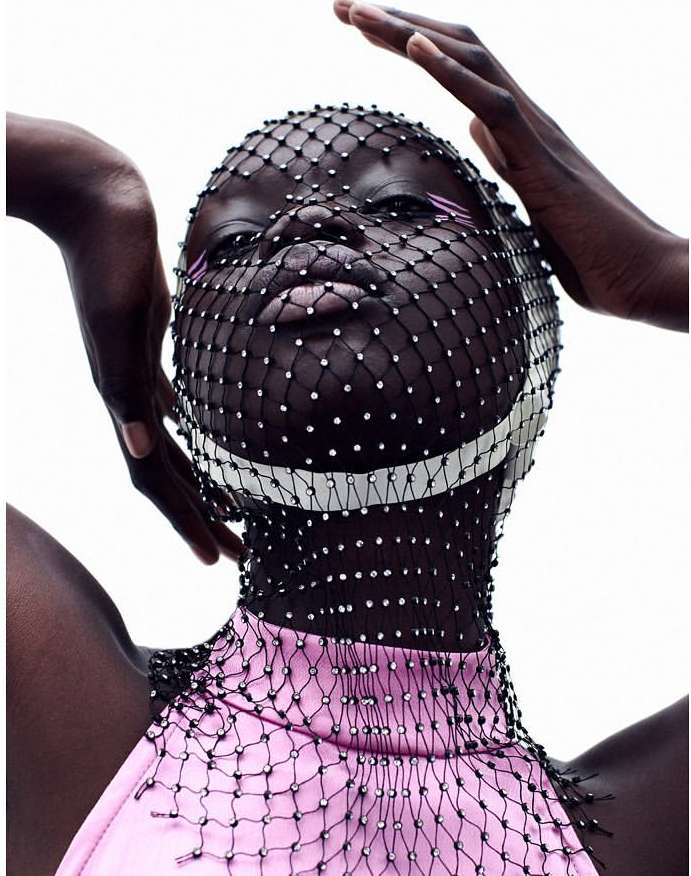 Fashion photo of a dark-skinned adult female posing with a rhinestone net covering her head and pink sleeveless top against a white background.