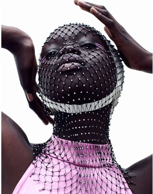 Fashion photo of a dark-skinned adult female posing with a rhinestone net covering her head and pink sleeveless top against a white background.