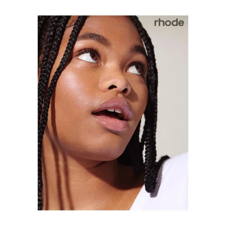 Close-up portrait of a young Black woman with braided hair and glossy lips looking upward against a plain white background.