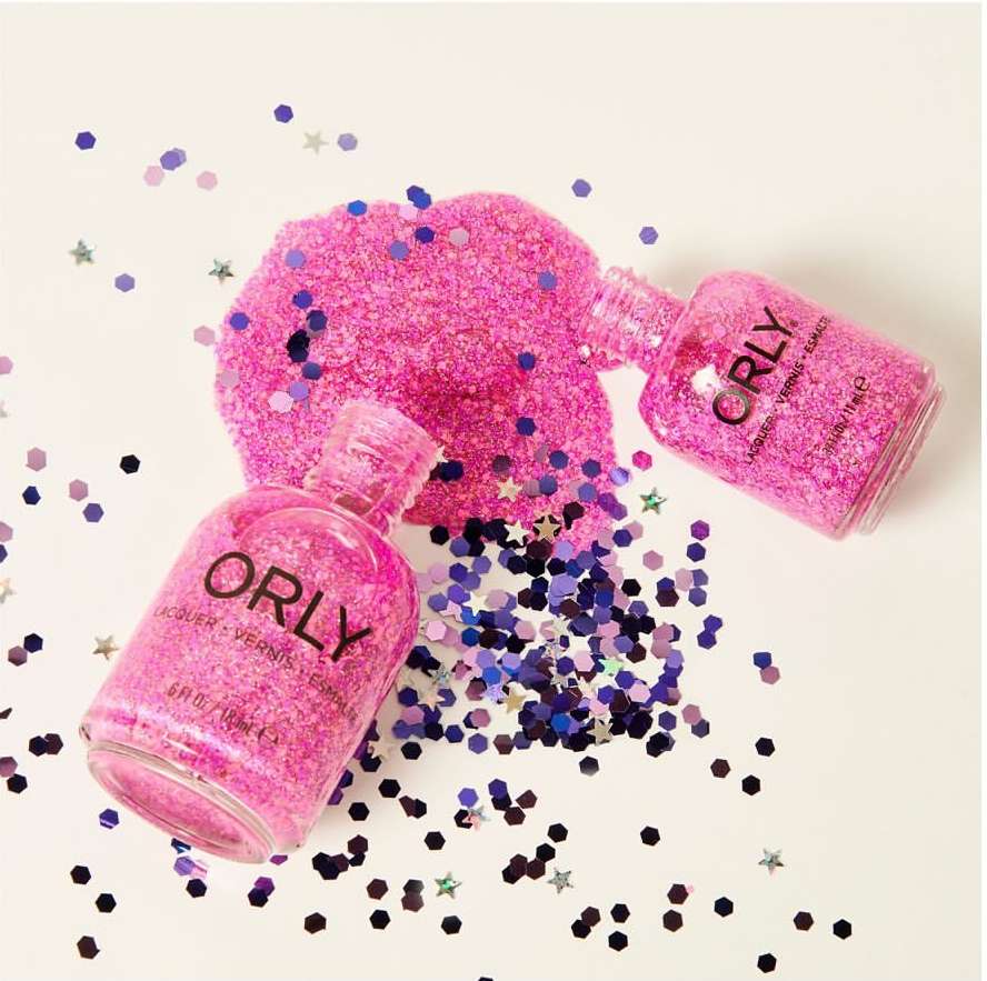 Two bottles of pink Orly nail polish surrounded by scattered purple and pink confetti, displayed on a white surface.