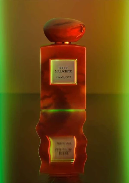 Elegant red perfume bottle on a reflective surface with golden and green lighting accents. Cosmetics and beauty product photography.