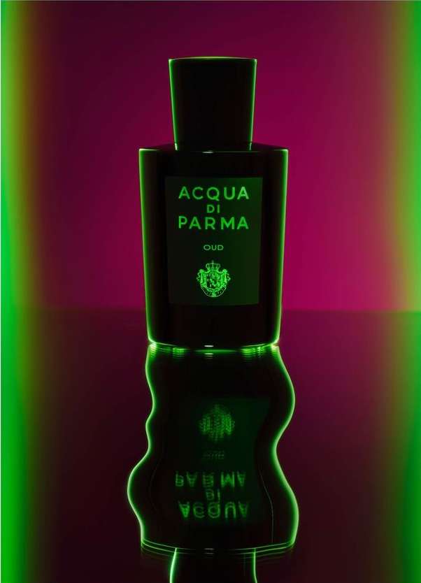 Elegant presentation of Acqua di Parma Oud perfume bottle against a vibrant magenta backdrop with glowing green accents and reflections.