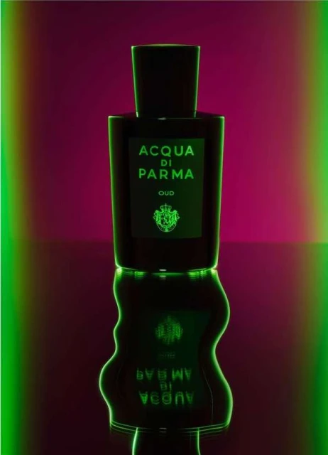 Elegant presentation of Acqua di Parma Oud perfume bottle against a vibrant magenta backdrop with glowing green accents and reflections.