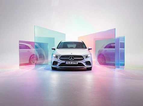 Silver Mercedes-Benz A-Class hatchback in a studio, set against a backdrop of translucent panels with iridescent color effects.