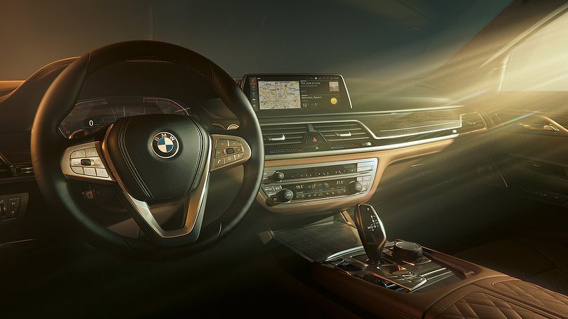 Interior of a BMW car featuring a black leather steering wheel with the BMW logo, dashboard display screen showing a map, and wood trim.