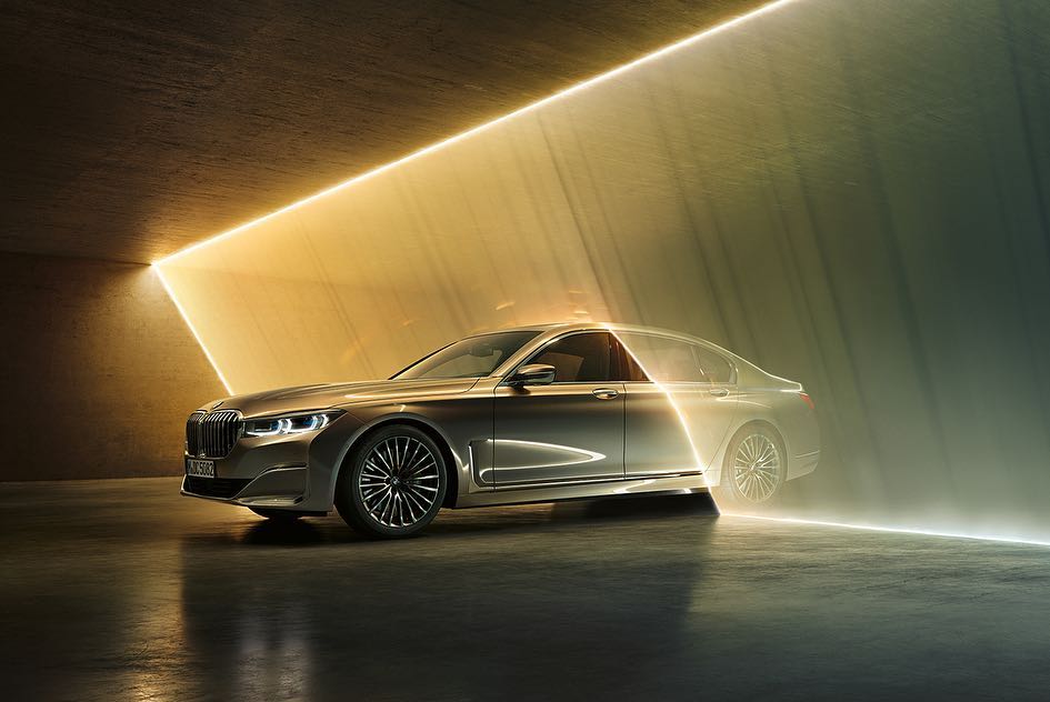 Silver BMW 7 Series parked indoors with bright geometric lighting, highlighting its sleek design and modern features.