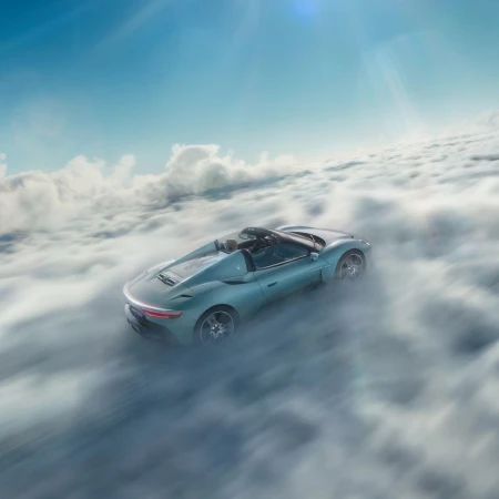 A light blue convertible car drives through a thick cloudscape under a blue sky, creating a dynamic and surreal automotive image.