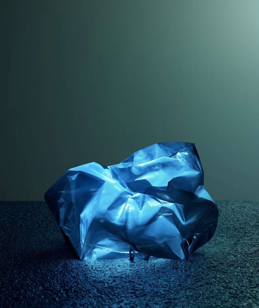 A blue crumpled plastic sheet sits on a textured blue surface against a blue-grey background, creating a textured, abstract image.