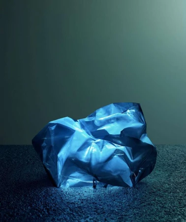 A blue crumpled plastic sheet sits on a textured blue surface against a blue-grey background, creating a textured, abstract image.