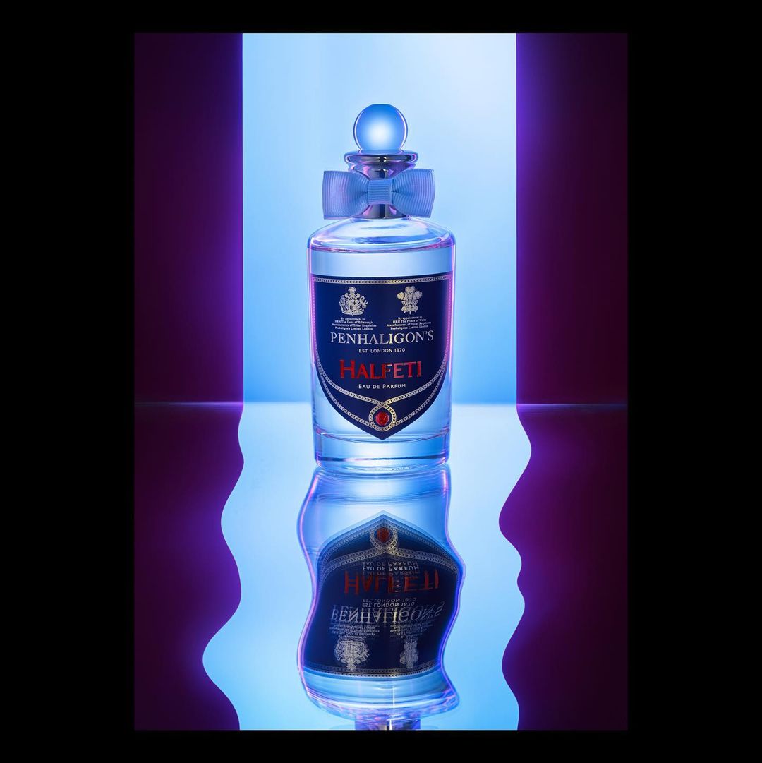 Penhaligon's Halfeti Eau de Parfum bottle in a studio product shot with a blue ribbon and a purple and blue backdrop.