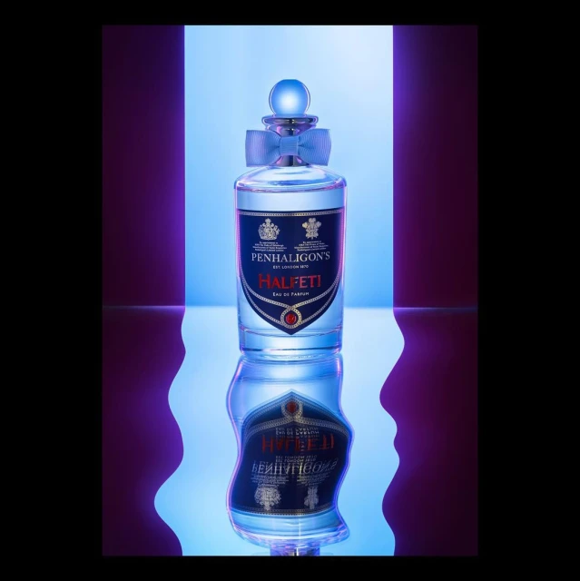 Penhaligon's Halfeti Eau de Parfum bottle in a studio product shot with a blue ribbon and a purple and blue backdrop.