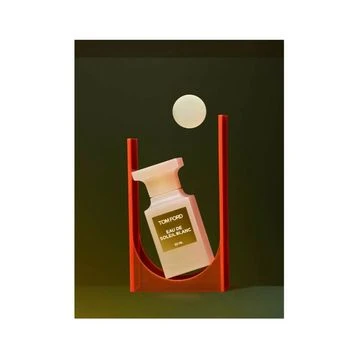 Tom Ford Eau de Soleil Blanc perfume bottle in a red curved display stand on a dark green background with a floating white orb.