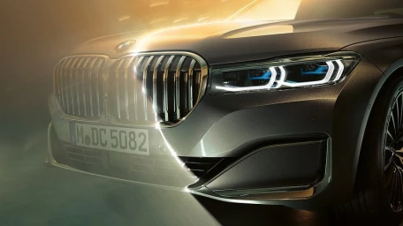 Close-up of a modern grey BMW luxury sedan front grille and LED headlight illuminated by a sharp beam of light against a dark background