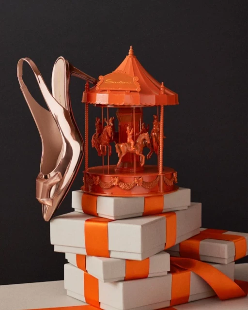 Elevated shot of rose gold high heel shoes artfully displayed on stacked white gift boxes with a miniature orange carousel.