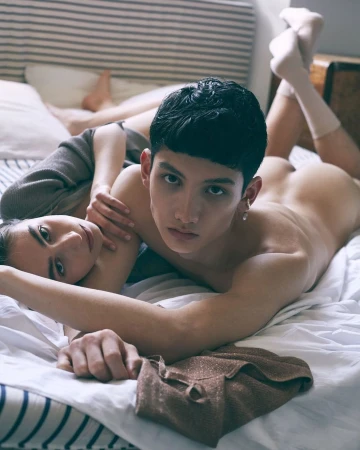 A young couple lying together on a white bed with striped pillows, photographed by Alessandro Burzigotti in Milan.