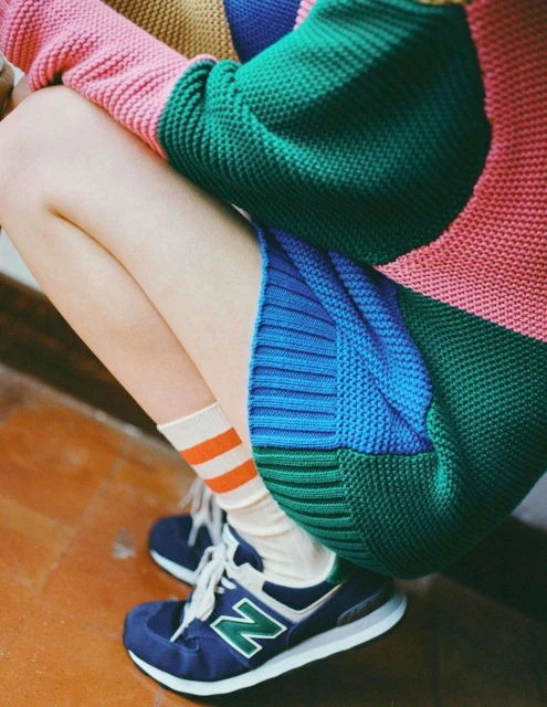 Knit striped sweater, blue sneakers, and socks with orange stripes on a person crouching on a terracotta-colored surface.
