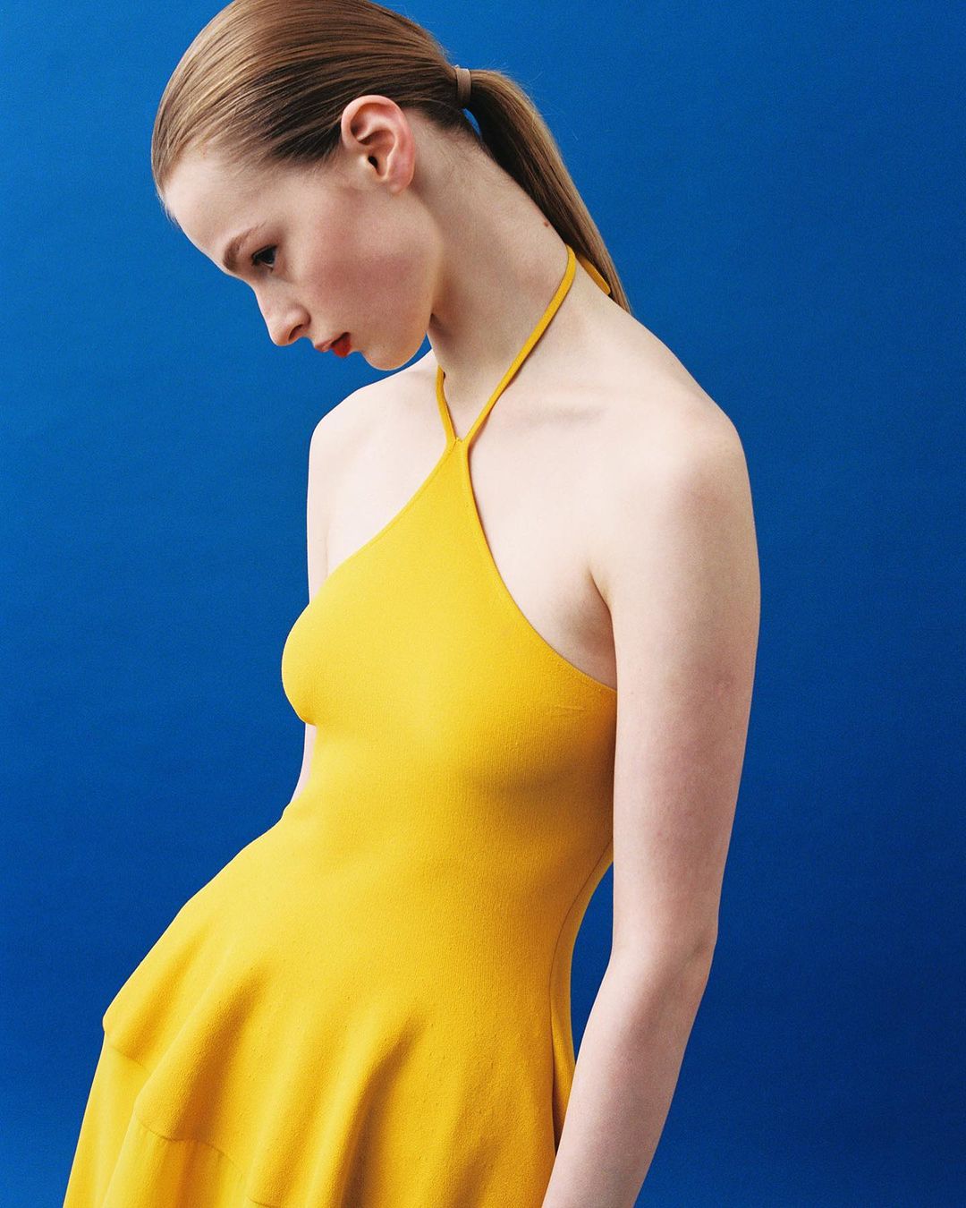 Model in a yellow halter dress against a vibrant solid blue background by Alessandro Burzigotti in Milan.