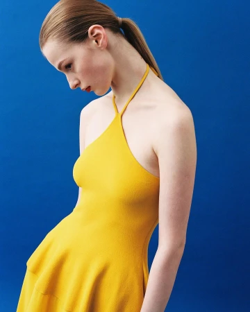 Model in a yellow halter dress against a vibrant solid blue background by Alessandro Burzigotti in Milan.
