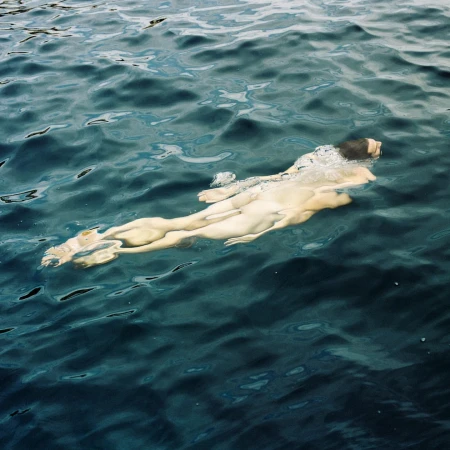 Figure swimming horizontally just beneath the dark blue surface of open water by Alessandro Burzigotti.