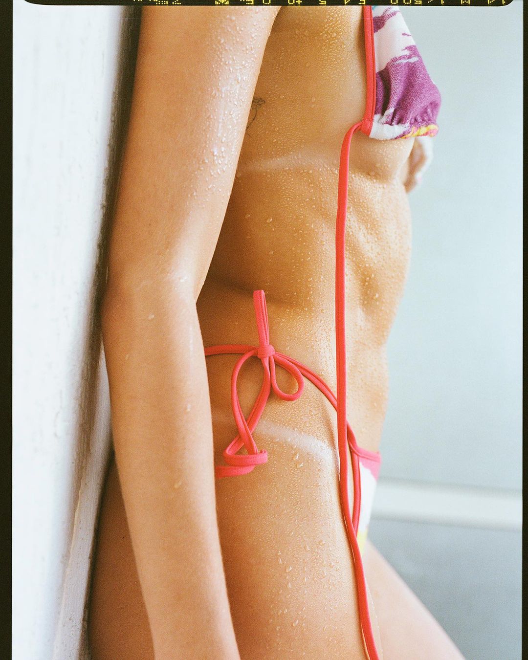 Close-up studio shot of a woman wearing a bikini, showcasing her tanned skin and the texture of water droplets on her body.