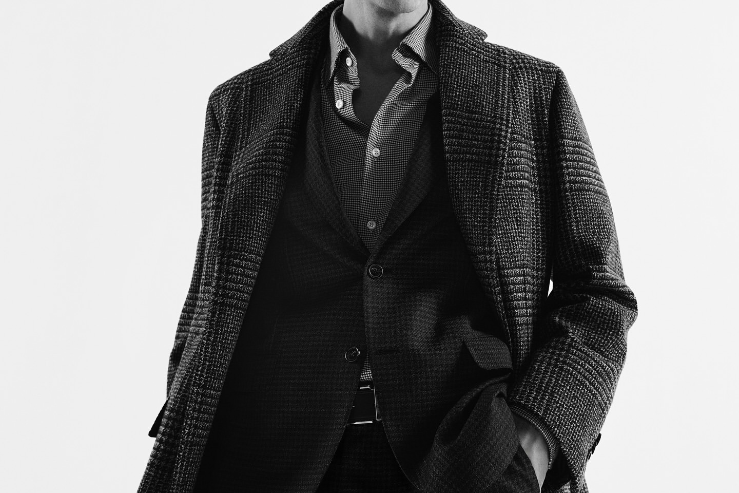 Man wearing a tweed coat, patterned button-up shirt, and suit jacket against a plain light background.