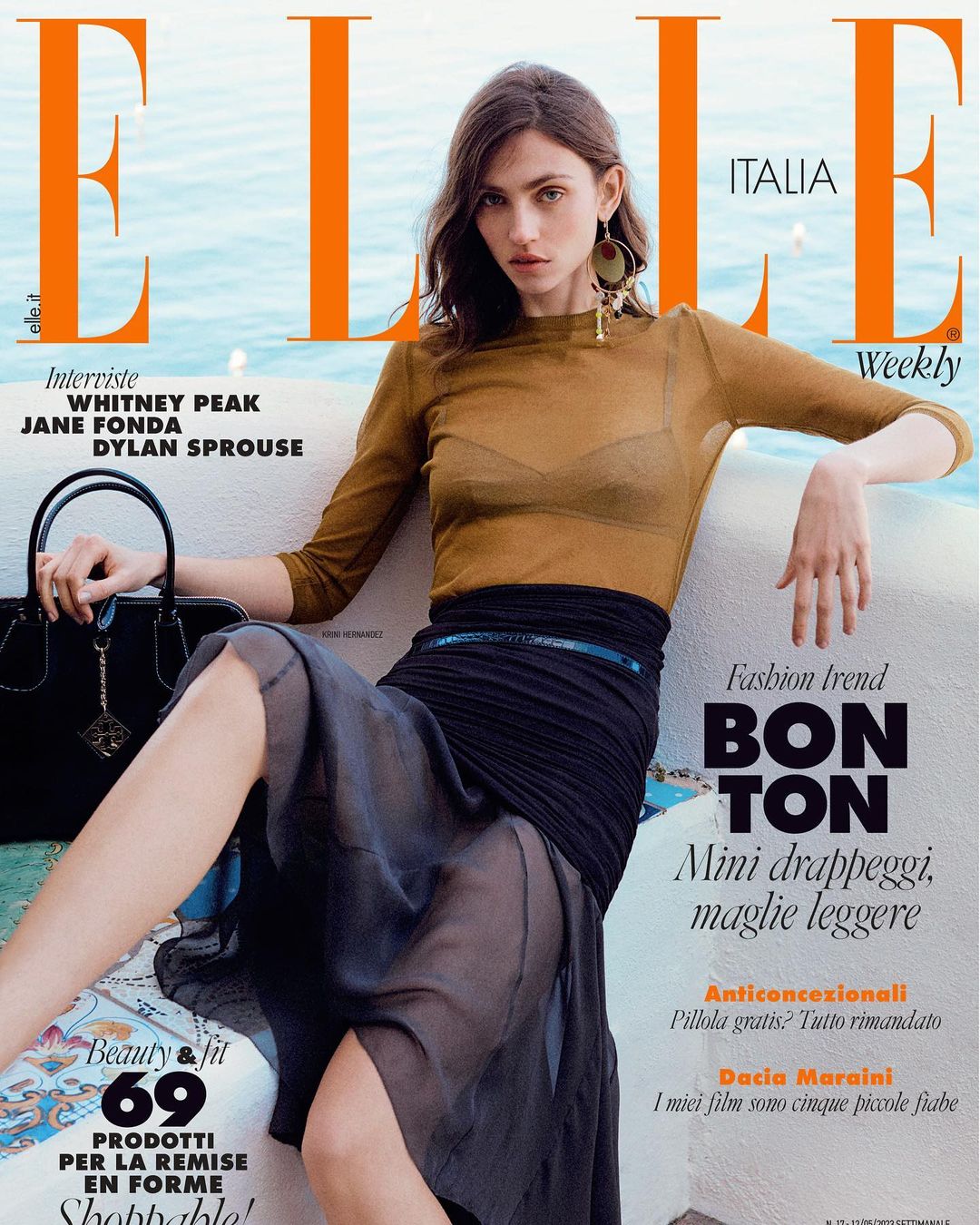 Elle Italia magazine cover featuring a posed adult female model with a sheer brown top, black skirt, and statement earrings against a blue background.