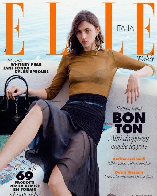 Elle Italia magazine cover featuring a posed adult female model with a sheer brown top, black skirt, and statement earrings against a blue background.