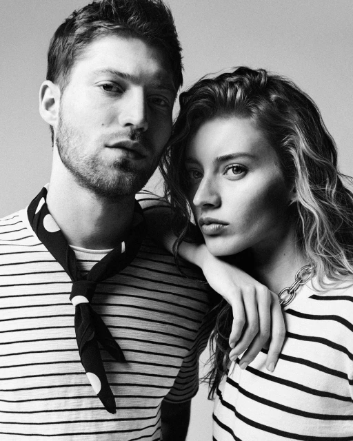 Black and white portrait of a stylish couple wearing black and white striped shirts and neckwear, posing in front of a neutral backdrop.