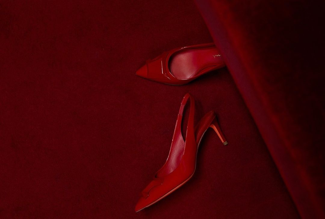 Pair of glossy red high heel shoes on a matching red velvet surface, one positioned toe-up and the other heel-up, fashion still life.