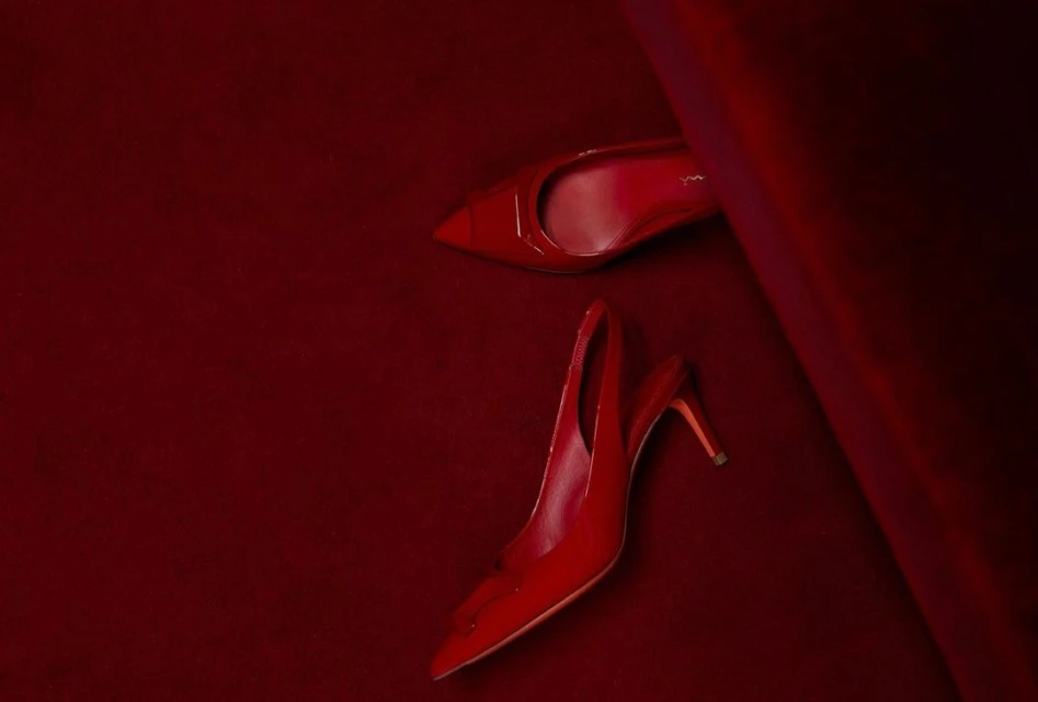 Pair of glossy red high heel shoes on a matching red velvet surface, one positioned toe-up and the other heel-up, fashion still life.