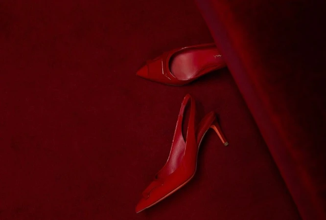 Pair of glossy red high heel shoes on a matching red velvet surface, one positioned toe-up and the other heel-up, fashion still life.