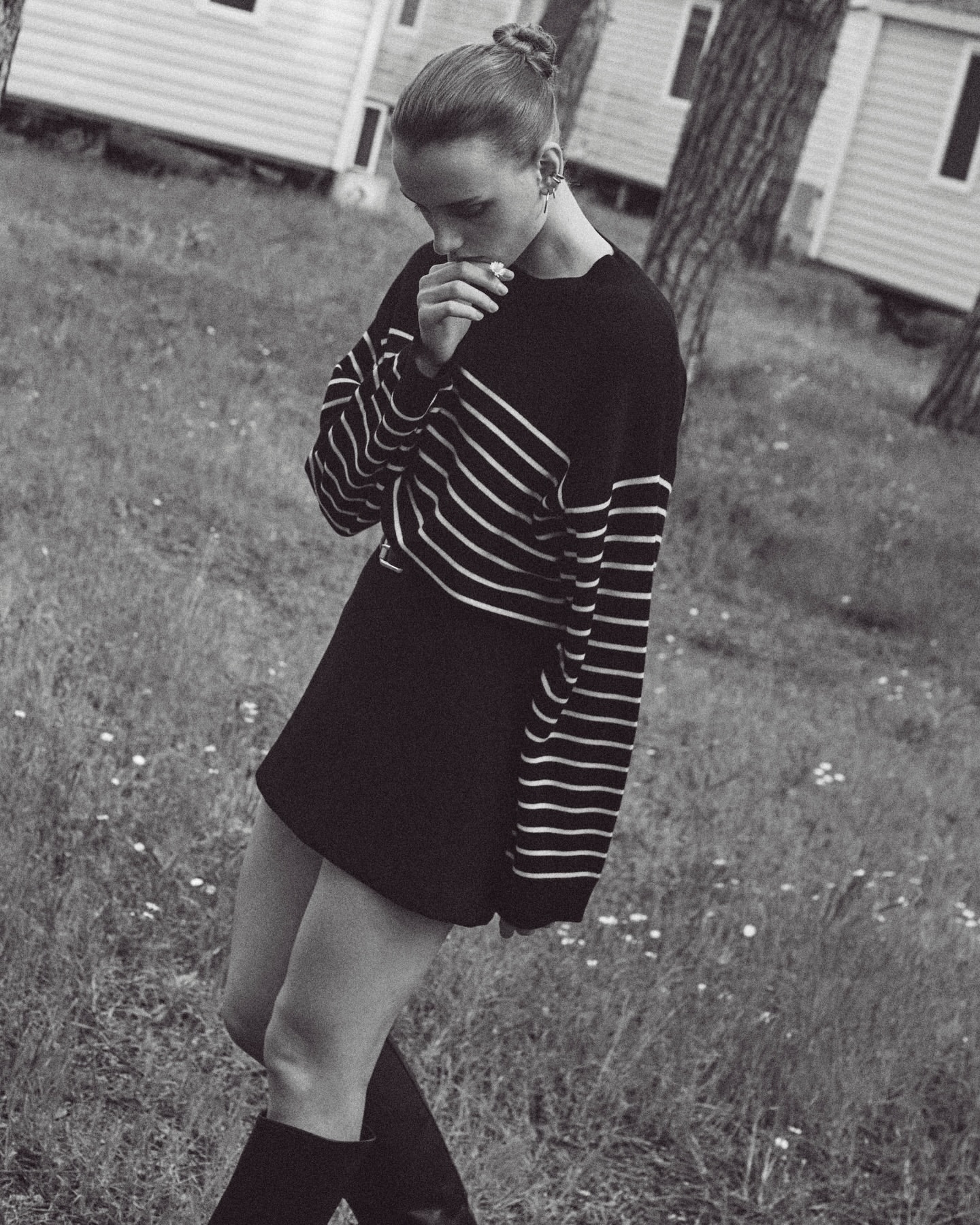 Monochrome full shot of a female in a black and white striped shirt, black skirt, and black boots standing in a grassy field.
