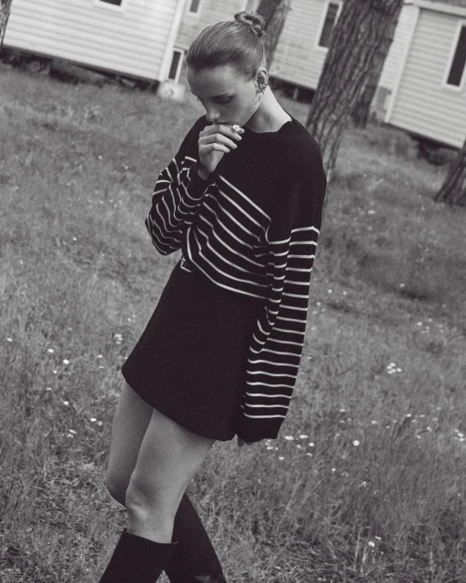 Monochrome full shot of a female in a black and white striped shirt, black skirt, and black boots standing in a grassy field.