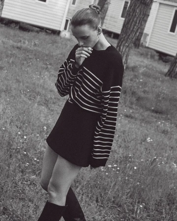 Monochrome full shot of a female in a black and white striped shirt, black skirt, and black boots standing in a grassy field.