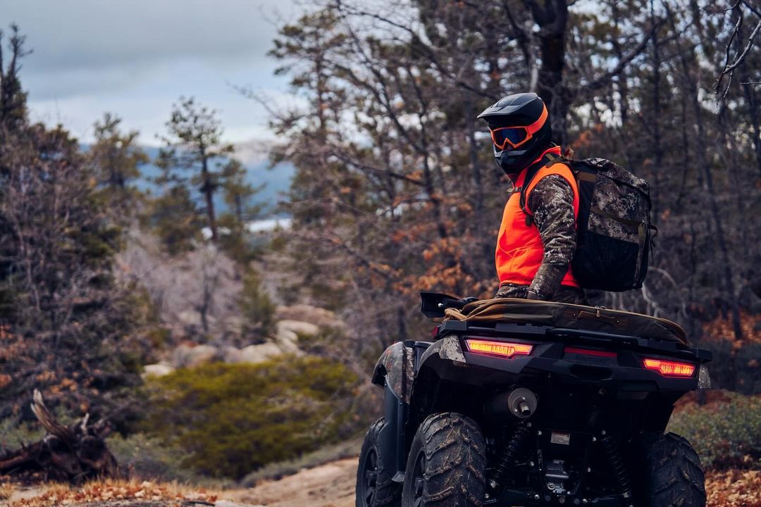 ATV rider in forest, helmet and orange vest, backpack, off-road vehicle, trees, outdoor recreation, forest landscape, travel concept.