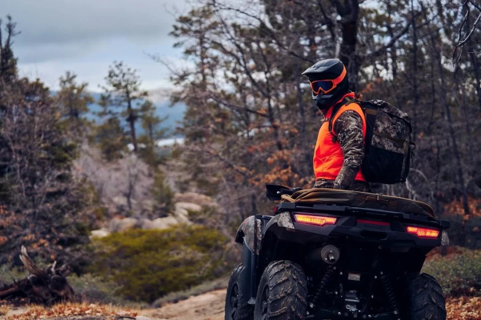 ATV rider in forest, helmet and orange vest, backpack, off-road vehicle, trees, outdoor recreation, forest landscape, travel concept.