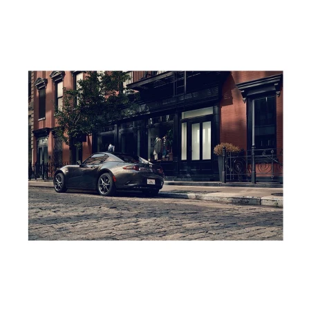 Grey Mazda Miata RF parked on a cobblestone street in front of a brick building with a shopfront during daytime, showcasing urban automotive photography.