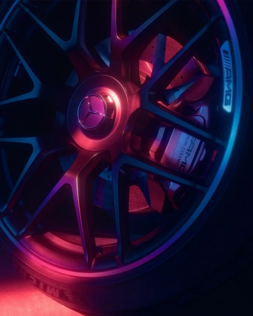 Close-up of a car wheel with the Mercedes-Benz logo in the center, showcasing the tire, rim, brake assembly, and vibrant color lighting.