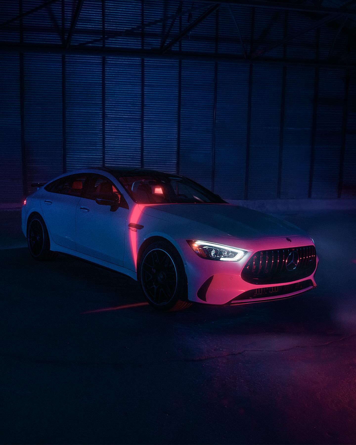 White Mercedes-Benz AMG GT 63 S under blue and pink neon lighting in an industrial setting. Automotive content for Visie search.