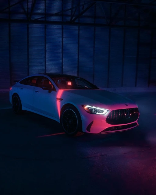 White Mercedes-Benz AMG GT 63 S under blue and pink neon lighting in an industrial setting. Automotive content for Visie search.