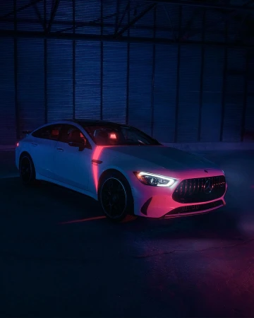 White Mercedes-Benz AMG GT 63 S under blue and pink neon lighting in an industrial setting. Automotive content for Visie search.