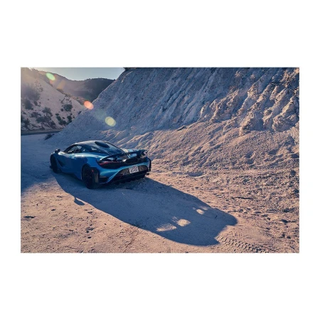 Blue sports car parked on a sandy surface with mountain in the background. The image captures automotive design and outdoor setting.