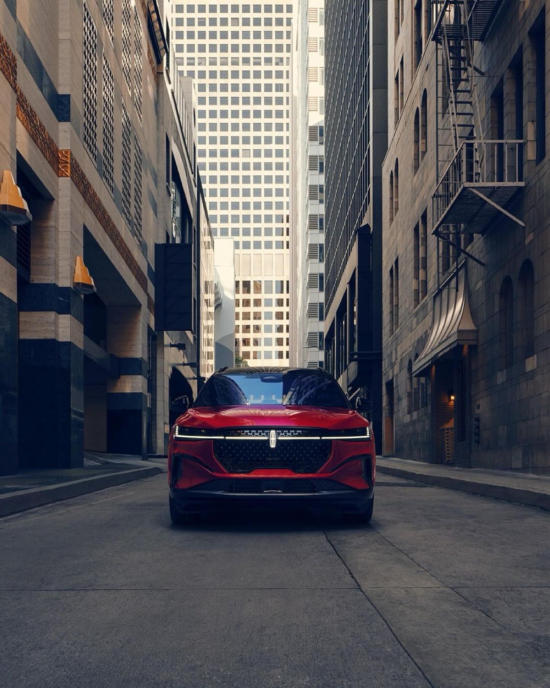 Red Lincoln sedan parked on a city street framed by tall buildings, showcasing a modern automotive design in an urban environment.