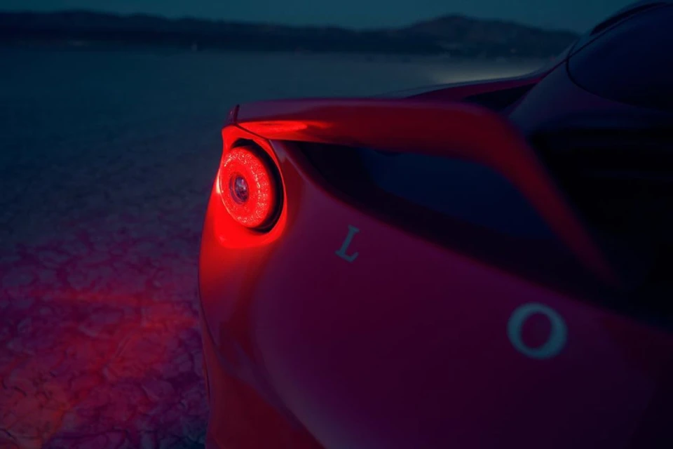 A close up of the red tail light on an automobile at dusk, with mountains faintly visible in the dark background.