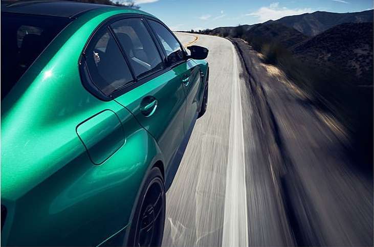 A bright green coupe races along a sunlit asphalt highway curving through mountains, showcasing speed and luxury on a scenic route.
