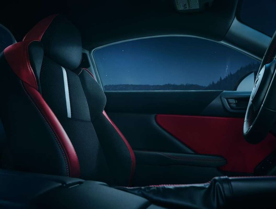 Interior view of a car with black and red seats and a dark night scene visible through the windows, creating a moody automotive image.